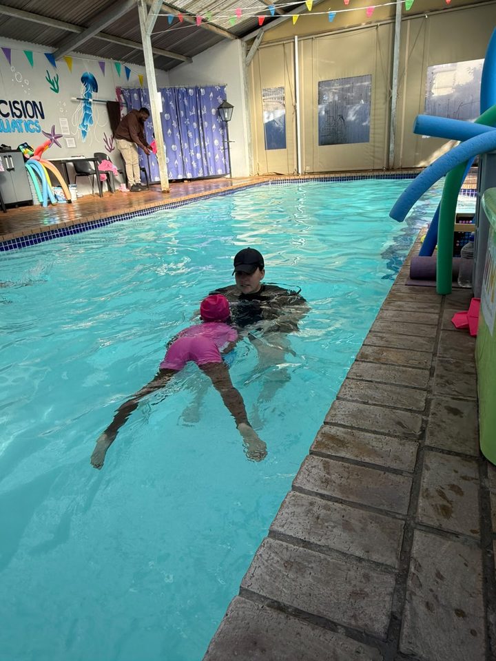 Instructor teaching a child to swim, Precision Aquatics wall signage visible