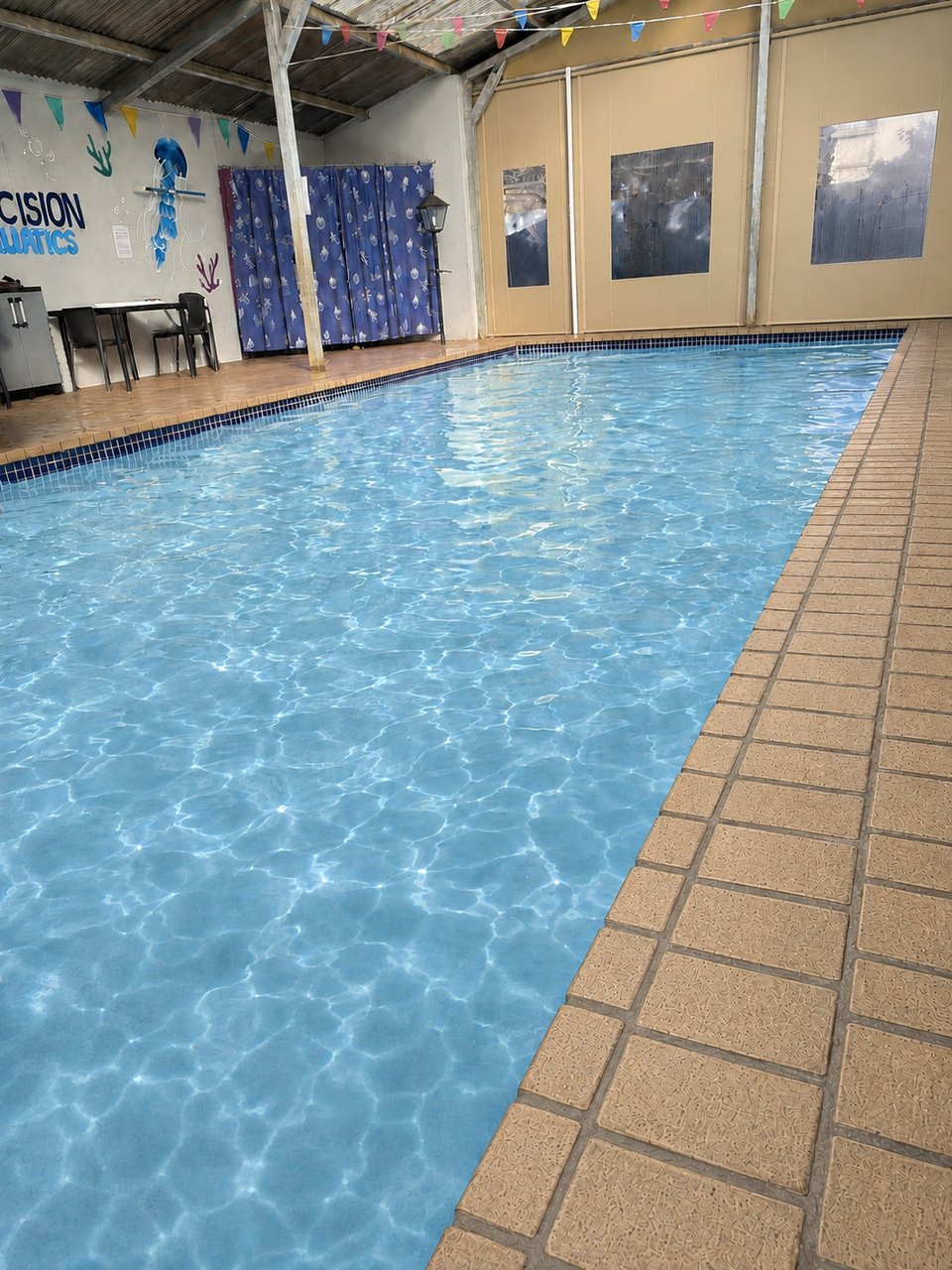 Indoor heated pool at Precision Aquatics with the Precision Aquatics wall signage and colourful bunting