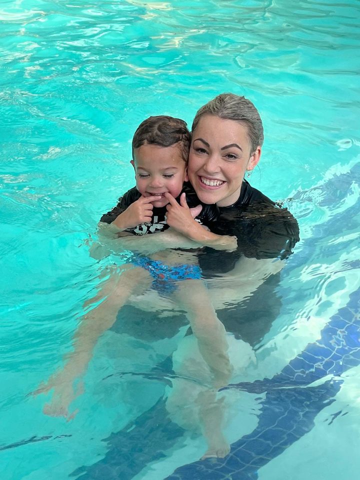 Instructor holding a smiling toddler in the pool